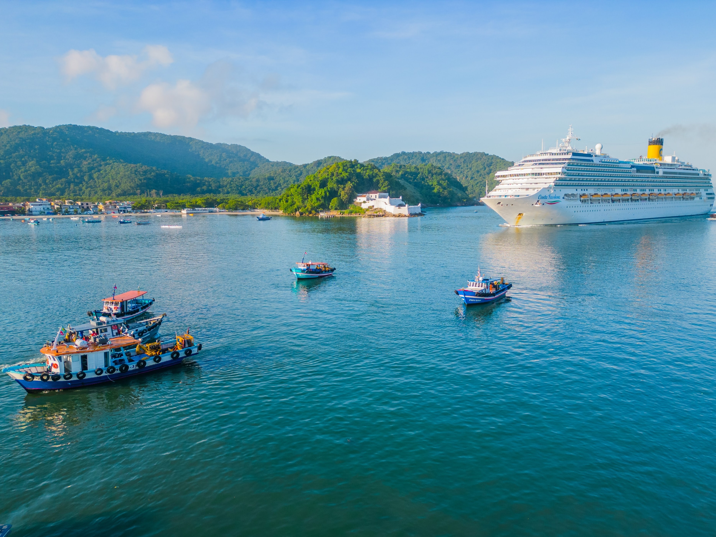 Embarcações de apoio no estuário de Santos, com a Fortaleza da Barra e um navio de cruzeiro ao fundo